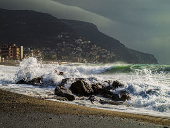 Waves splashing on rocks at shore against sky