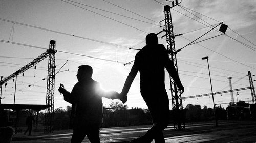 Silhouette man and woman standing on electricity pylon against sky