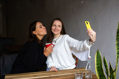 Two women friends have fun outdoors in cafe and take a selfie on a smartphone