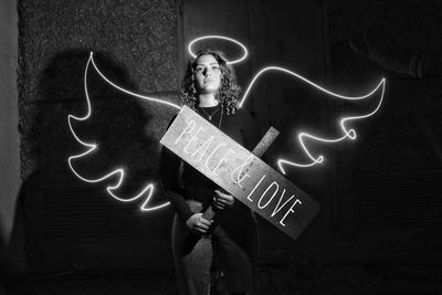 Digital composite image of woman holding information sign with wings and halo against wall