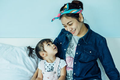 Smiling woman with daughter sitting on bed at home