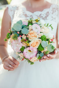 Midsection of bride holding rose bouquet