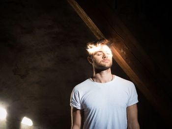 Young man standing in light with closed eyes