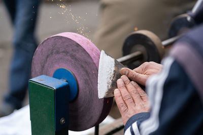 Master sharpens ax on electric sharpener with bright sparks and holds blade with his brutish fingers