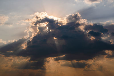 Low angle view of sunlight streaming through clouds