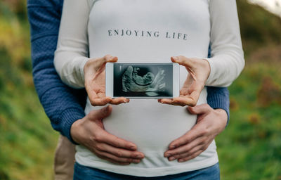 Midsection of pregnant woman with man holding mobile phone