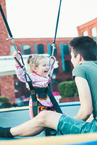 Brother playing with sister on swing at playground