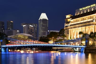 Illuminated bridge over river by buildings against sky at night