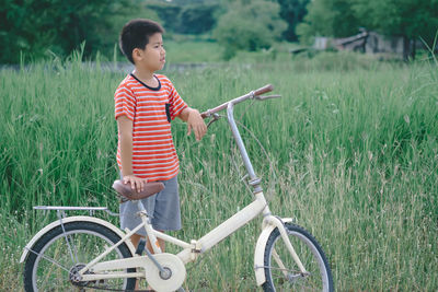 Boy standing with bicycle on field