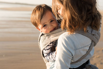 Mother carrying son while standing at beach