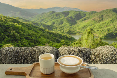 Coffee and cup on table against mountains