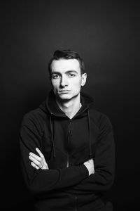 Portrait of young man with arms crossed against black background