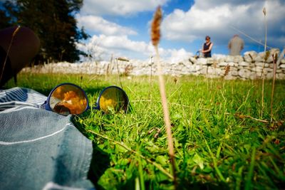 Surface level of sunglasses and clothes on grass with couple in background