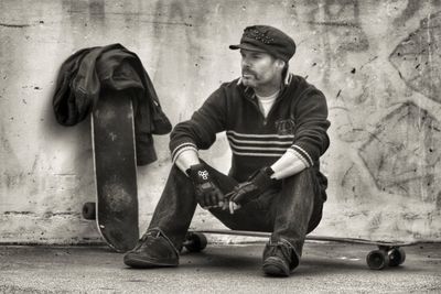 Man sitting on skateboard against wall