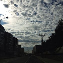 Road passing through city against cloudy sky