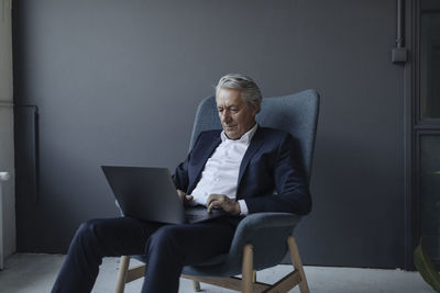 Senior businessman sitting in armchair using laptop