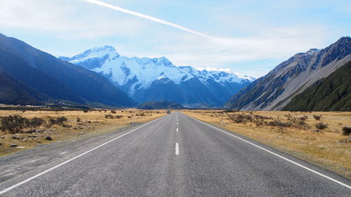 Road leading towards snowcapped mountains against sky