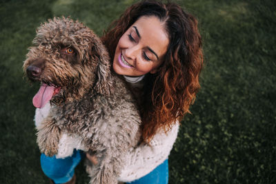 High angle view of smiling woman holding dog on grassy land