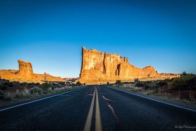 Road leading towards rock formations against blue sky