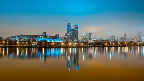 Illuminated buildings by river against sky at night