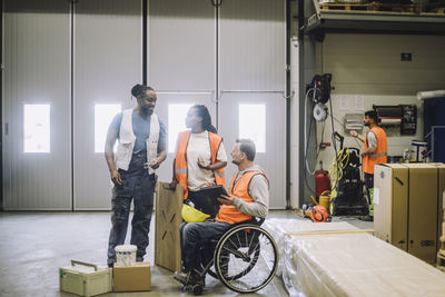 Carpenter sitting on wheelchair discussing with colleagues in warehouse