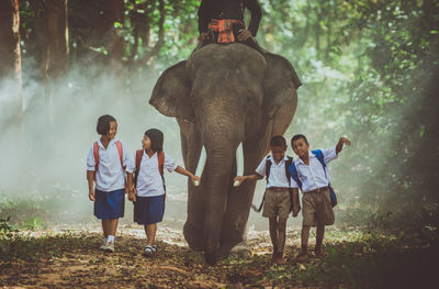 School children walking by elephant in forest