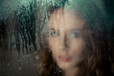 Close-up portrait of woman seen through wet window in rainy season