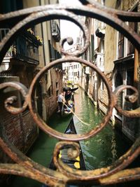 Man standing on gondola sailing on canal amidst buildings seen through wrought iron