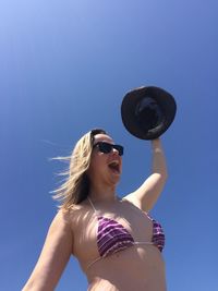 Low angle view of woman wearing bikini standing against clear sky