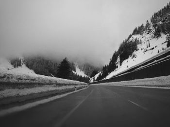 Road by mountains against clear sky during winter