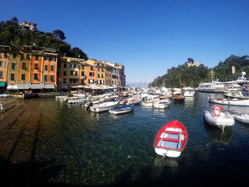 Boats moored in river by buildings against clear sky