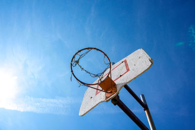 Looking up at worn out basketball hoop and wooden backboard with blue sky as backdrop