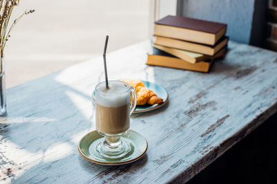 Latte in a tall glass against the background of a stack of books.the drink is on the table in a cafe