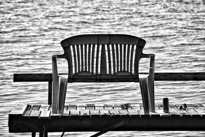 Empty chairs on pier by sea