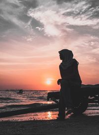 Woman wearing hijab looking at sea against sky during sunset