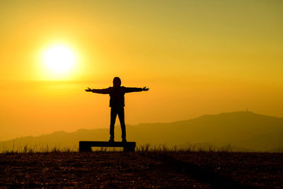 Silhouette man standing on field against sky during sunset