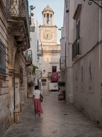 Rear view of woman walking amidst buildings in locorotondo, italy.