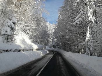 Snow covered road by trees against sky