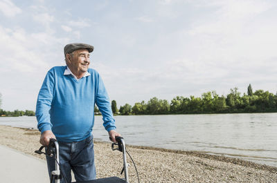 Smiling senior man strolling with wheeled walker at riverside