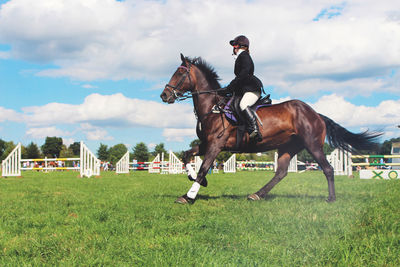 Low angle view of woman riding horse on field against cloudy sky