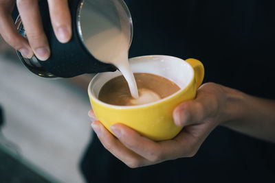 Midsection of woman pouring milk in coffee cup