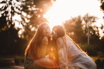 Lesbian couple blowing bubbles while sitting in park during summer