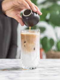 Close-up of hand pouring drink in glass on table