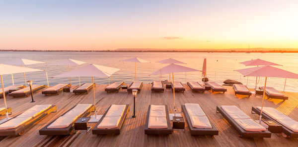 High angle view of deck chairs with parasols on pier over sea against sky during sunset