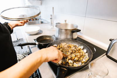 Heap of tasty mollusks with shells frying in hot black frying pan on electric cooker in light kitchen at home