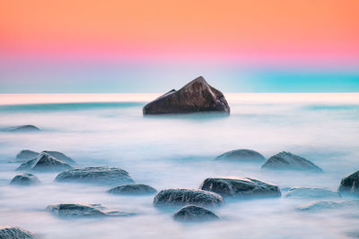 Rocks in sea against sky during sunset