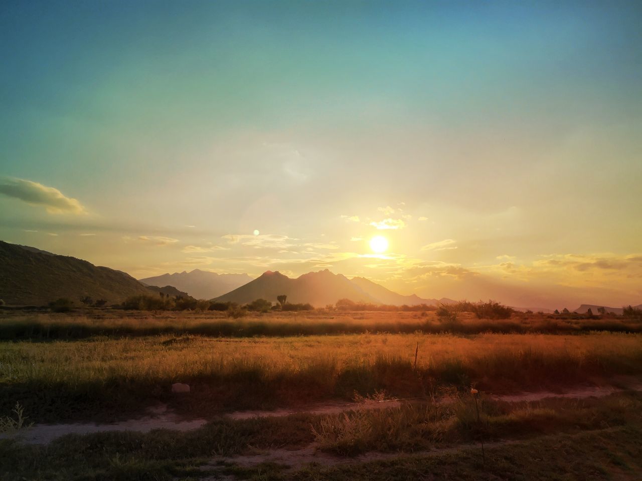 tranquil scene, landscape, sunset, sun, tranquility, scenics, mountain, beauty in nature, sky, field, nature, sunlight, grass, mountain range, idyllic, sunbeam, non-urban scene, horizon over land, cloud - sky, rural scene