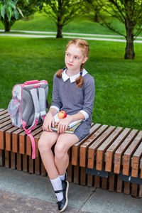 Full length of girl looking away while sitting on bench in park