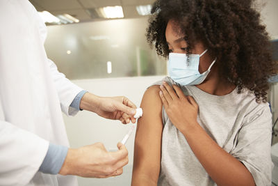 Girl with protective face mask taking covid-19 vaccination at hospital