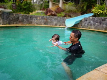 Father assisting toddler daughter swimming in pool